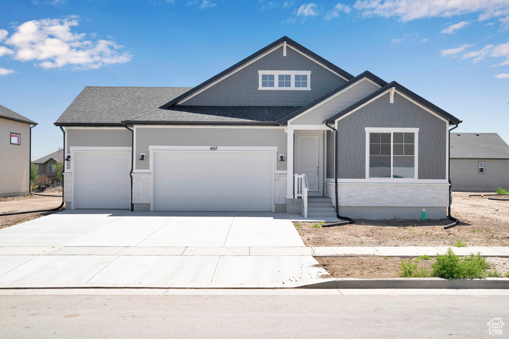 View of front of home featuring an attached garage, concrete driveway, a shingled roof, and stone siding