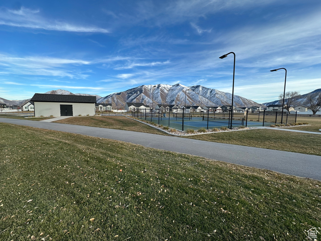 Surrounding community featuring a lawn, a tennis court, fence, and a mountain view