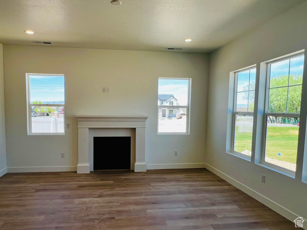 Unfurnished living room with baseboards, wood finished floors, a fireplace, and plenty of natural light