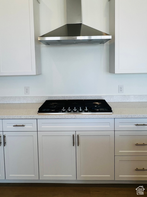 Kitchen with white cabinetry, light countertops, gas stovetop, and wall chimney exhaust hood