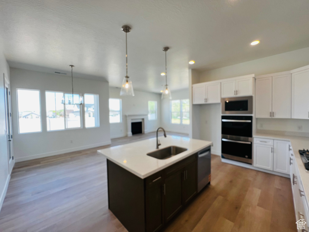 Kitchen featuring white cabinets, a sink, appliances with stainless steel finishes, light countertops, and a fireplace