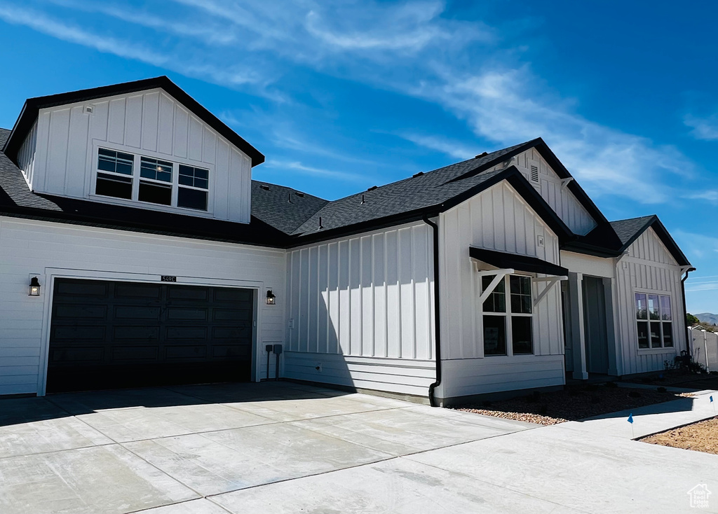 View of side of property with driveway, board and batten siding, a shingled roof, and an attached garage