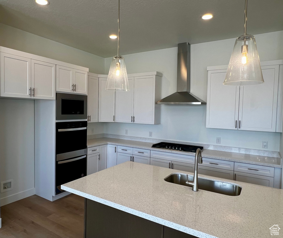 Kitchen featuring wood finished floors, white cabinets, black appliances, a sink, and wall chimney exhaust hood