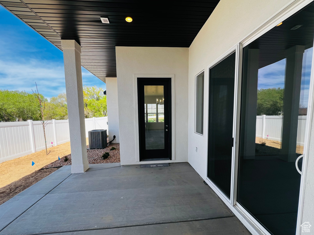 View of exterior entry with a patio, fence, stucco siding, and central air condition unit