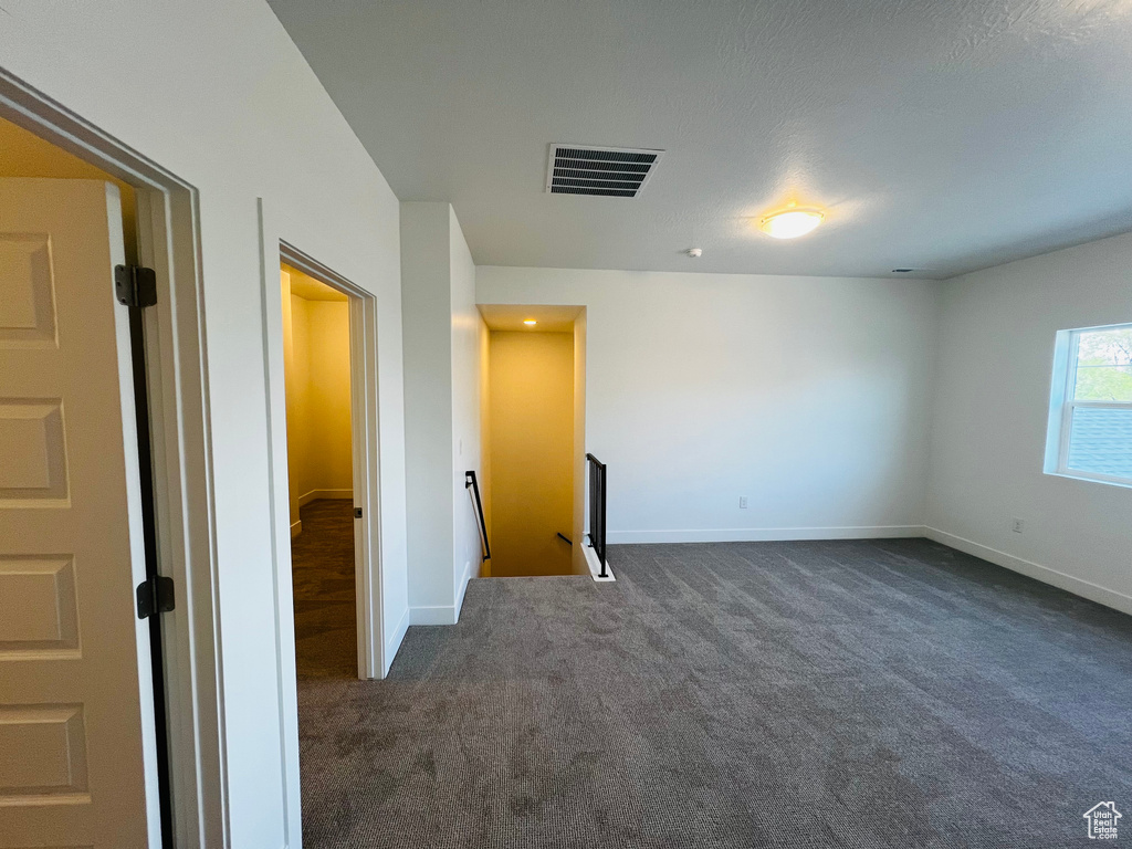 Unfurnished room featuring dark colored carpet, visible vents, and baseboards