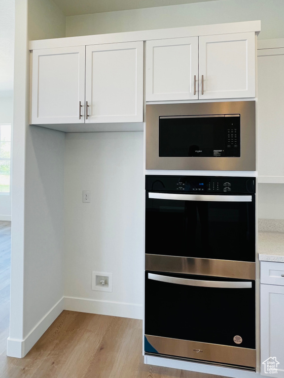 Kitchen featuring white cabinetry, built in microwave, dobule oven black, and light wood-type flooring