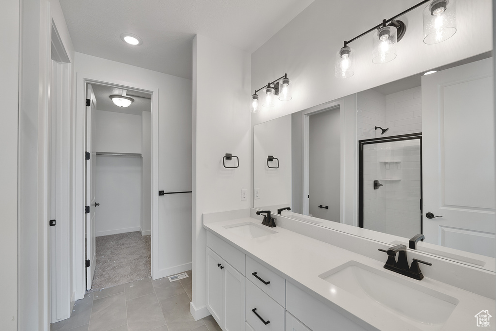 Bathroom featuring tiled shower, double vanity, a walk in closet, tile patterned flooring, and recessed lighting