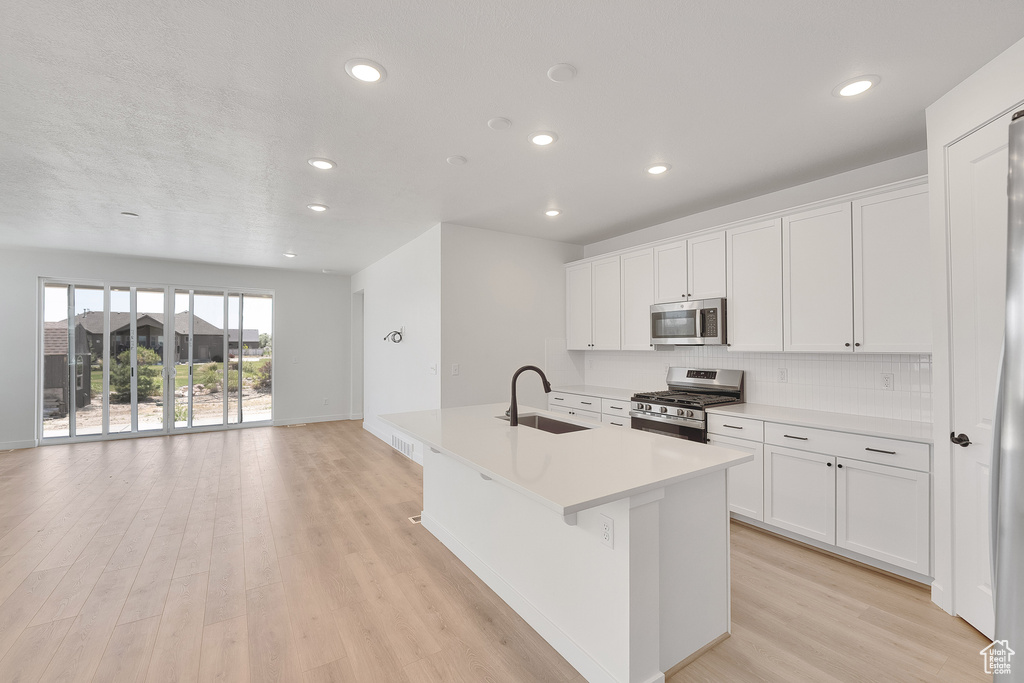Kitchen with stainless steel appliances, an island with sink, recessed lighting, light wood finished floors, and white cabinets