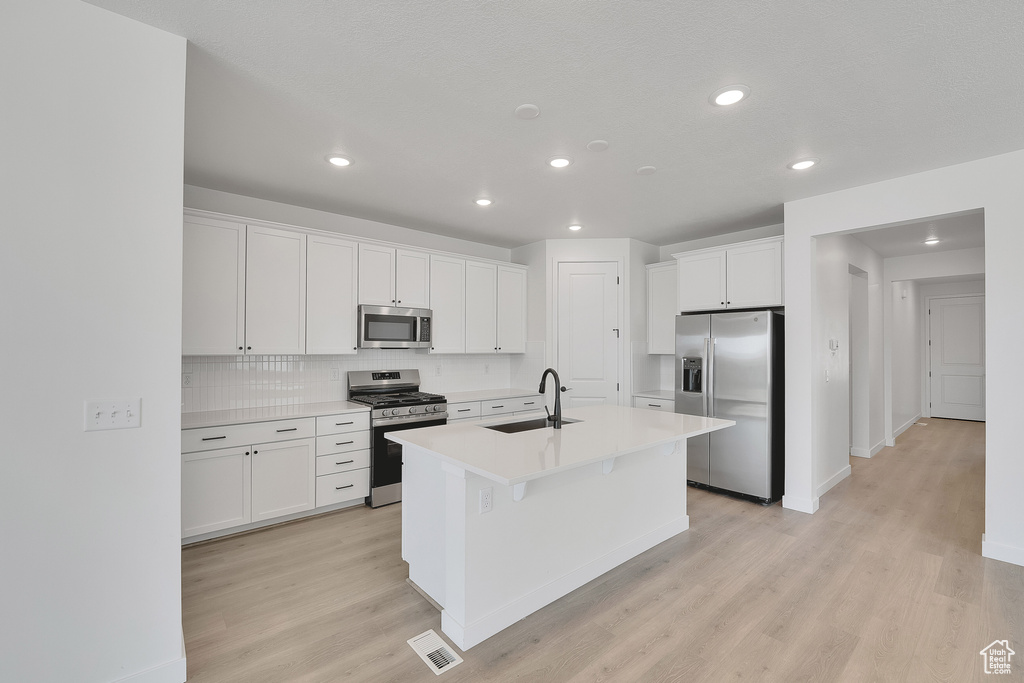 Kitchen with appliances with stainless steel finishes, light wood-style floors, a center island with sink, white cabinets, and backsplash