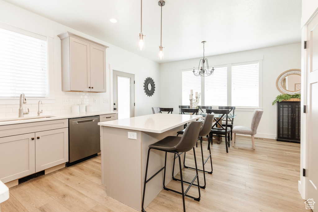 Kitchen with light wood finished floors, a sink, a breakfast bar, a kitchen island, and dishwasher