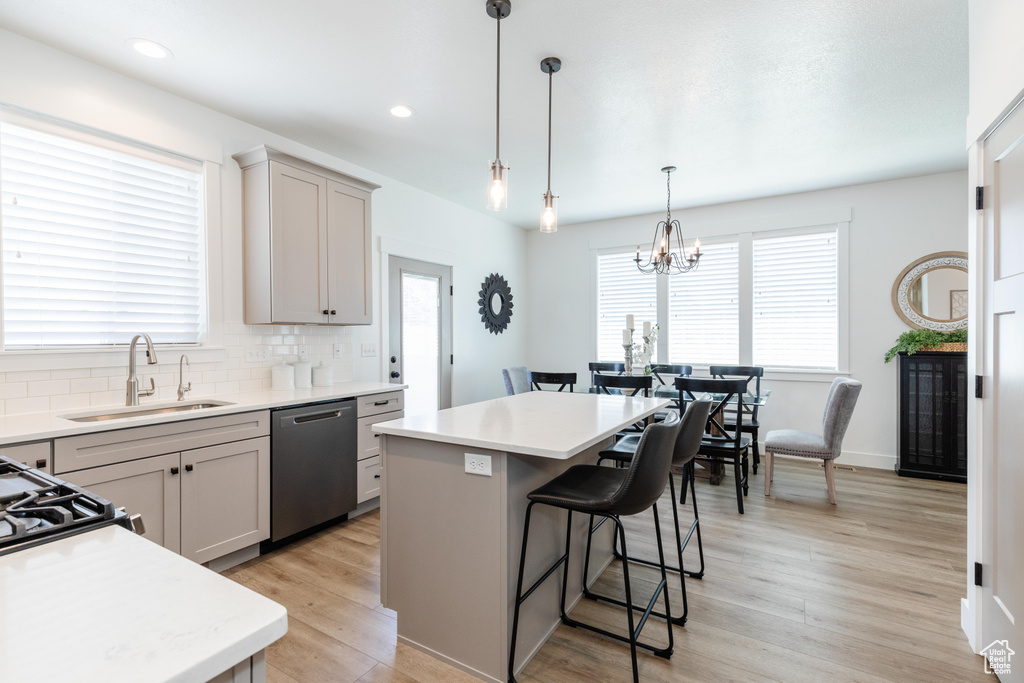 Kitchen featuring stainless steel dishwasher, a kitchen island, a kitchen breakfast bar, light countertops, and a sink