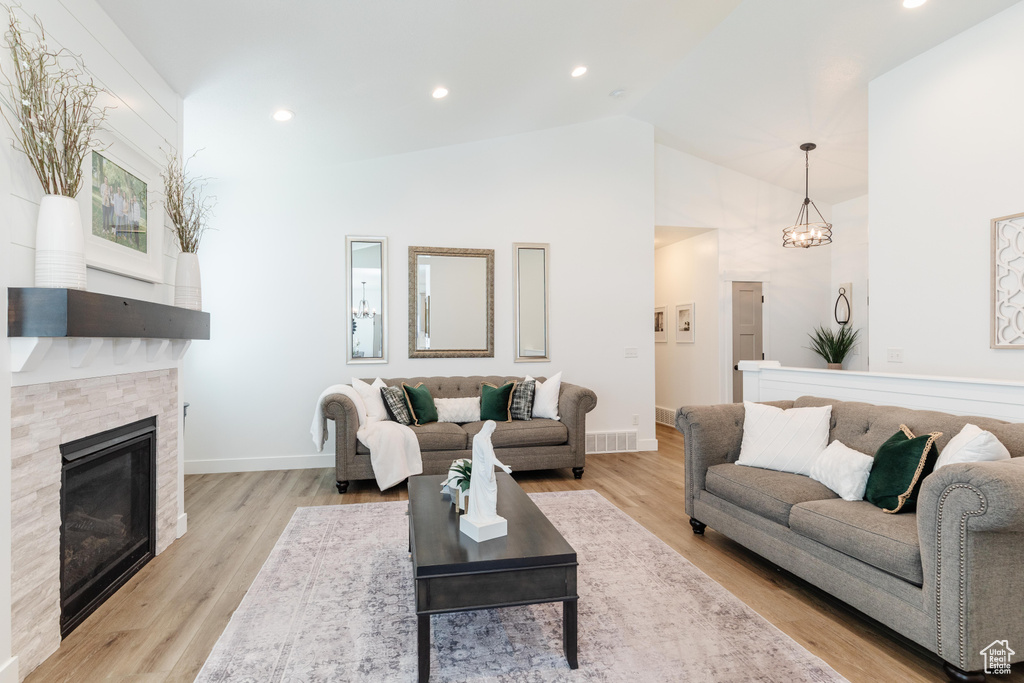 Living room featuring visible vents, baseboards, a stone fireplace, high vaulted ceiling, and a notable chandelier