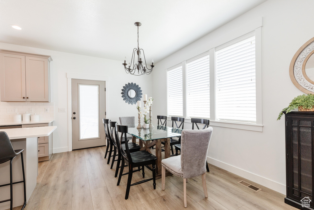 Dining room with visible vents, light wood-style flooring, a chandelier, and baseboards