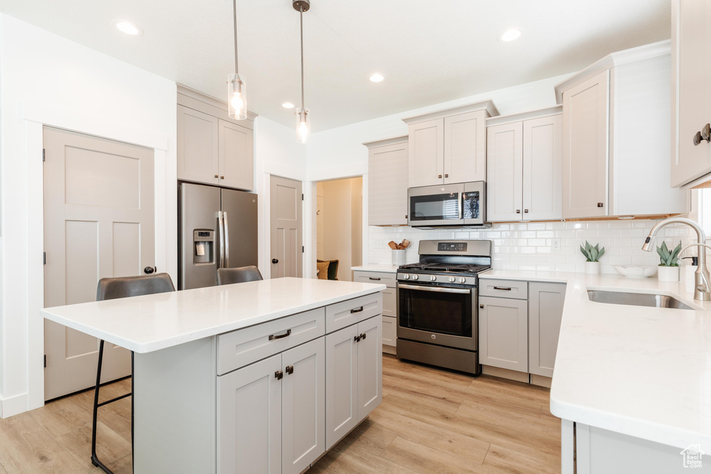 Kitchen with a sink, a center island, a breakfast bar, backsplash, and appliances with stainless steel finishes