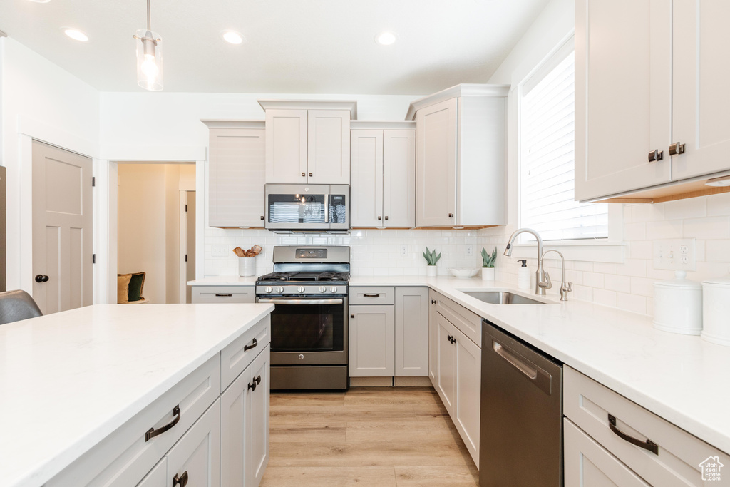 Kitchen featuring a sink, light wood-style floors, light countertops, hanging light fixtures, and appliances with stainless steel finishes
