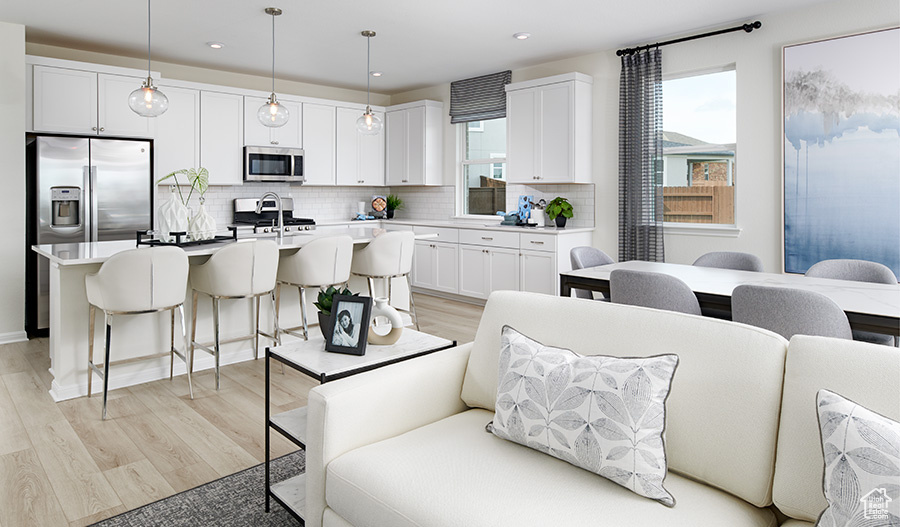 Kitchen featuring decorative backsplash, a breakfast bar, appliances with stainless steel finishes, white cabinetry, and open floor plan