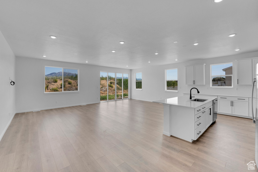 Kitchen featuring open floor plan, recessed lighting, stainless steel dishwasher, a kitchen island with sink, and white cabinets