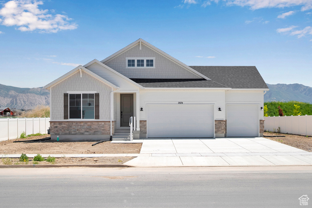 Craftsman-style house with a mountain view, stone siding, a garage, concrete driveway, and a shingled roof