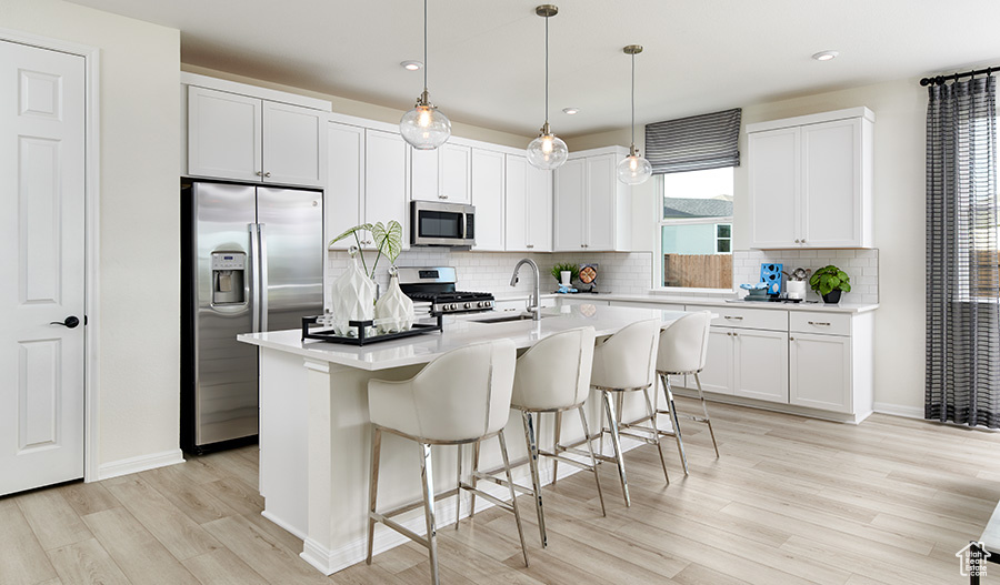 Kitchen featuring tasteful backsplash, a sink, stainless steel appliances, light countertops, and light wood-type flooring