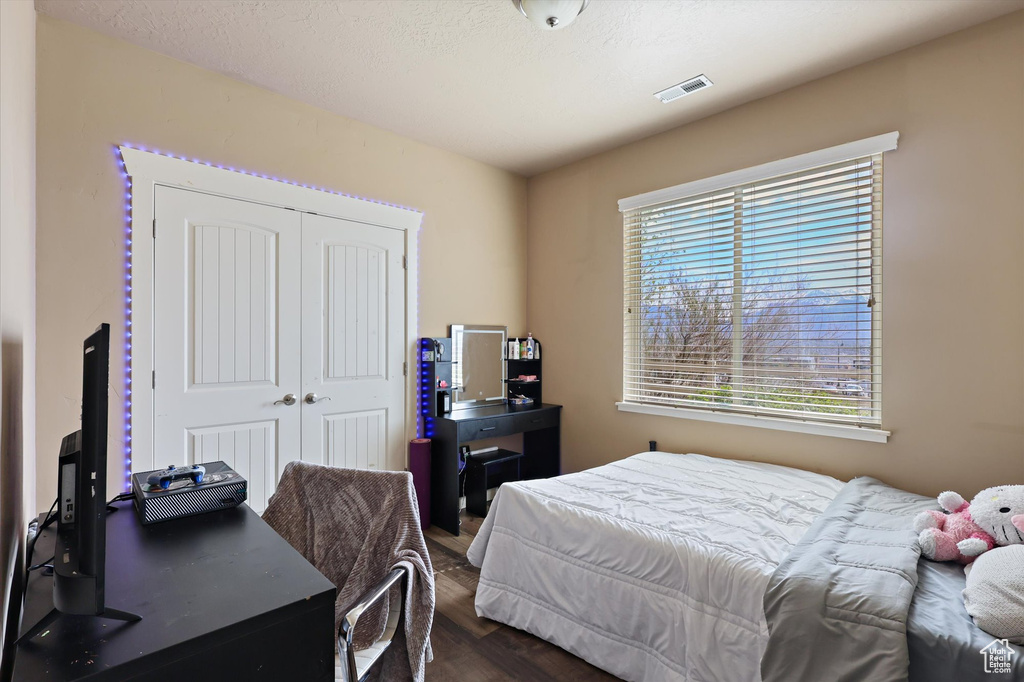 Bedroom with a closet, dark wood-style flooring, and visible vents