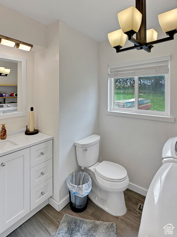 Bathroom with baseboards, toilet, wood finished floors, vanity, and a notable chandelier
