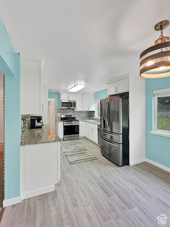 Kitchen featuring light wood finished floors, light stone countertops, stainless steel appliances, white cabinetry, and baseboards