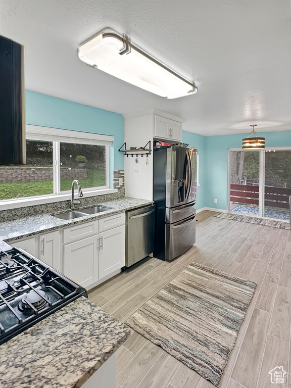 Kitchen with light stone counters, white cabinets, a sink, appliances with stainless steel finishes, and wood finish floors