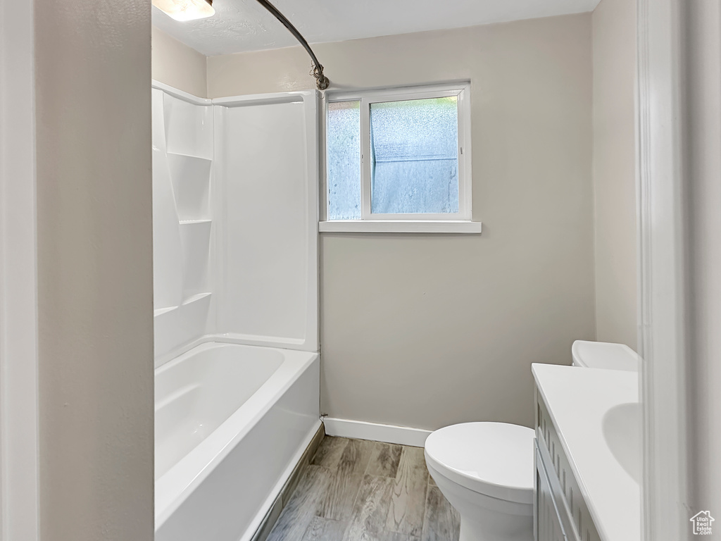 Full bathroom featuring baseboards, toilet, wood finished floors, vanity, and  shower combination