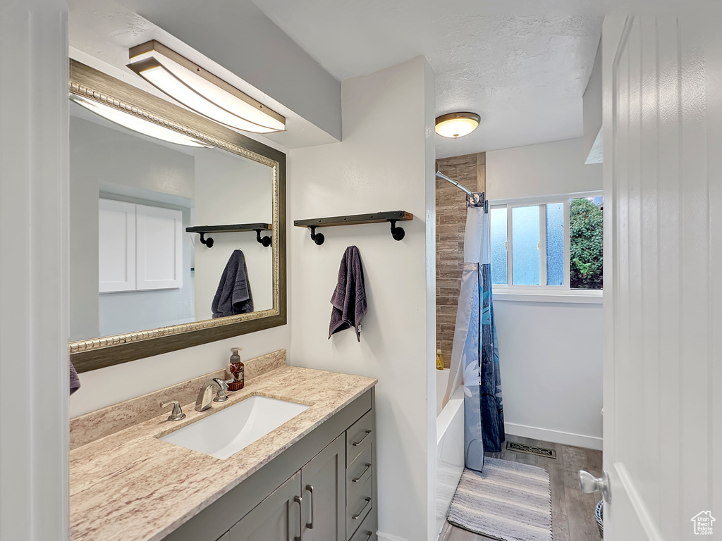 Bathroom featuring shower / bathtub combination with curtain, vanity, visible vents, baseboards, and wood finished floors