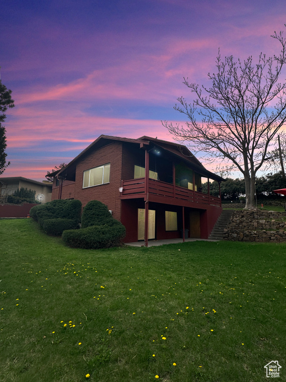 Back of house at dusk with a lawn, a wooden deck, a patio, and brick siding