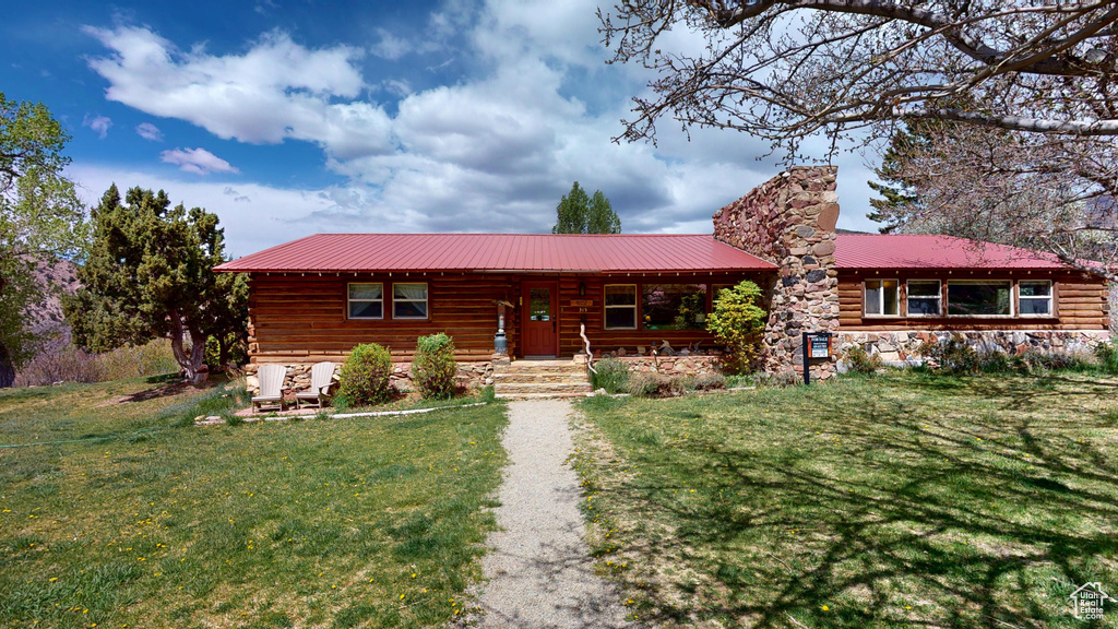 View of front facade featuring a front lawn, metal roof, a chimney, log siding, and a porch