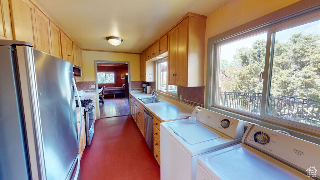Kitchen with decorative backsplash, a sink, light countertops, stainless steel appliances, and washer and clothes dryer