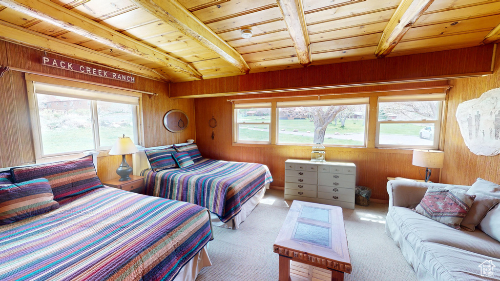 Carpeted bedroom featuring wooden walls, wooden ceiling, multiple windows, and beamed ceiling