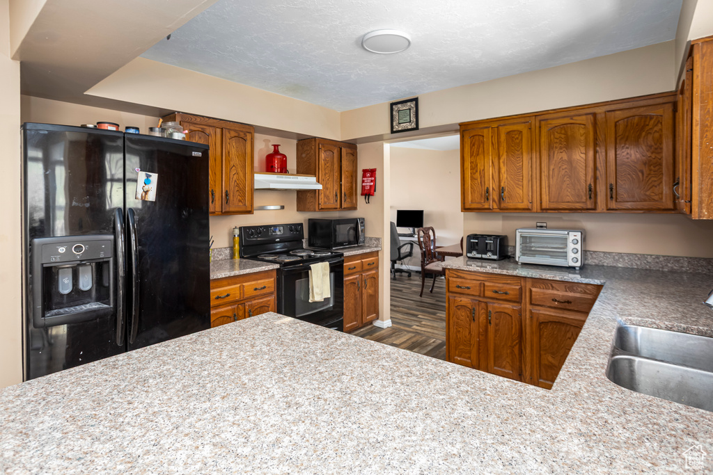 Kitchen featuring a toaster, under cabinet range hood, brown cabinets, black appliances, and a sink