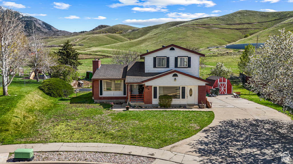 View of front of home with an outdoor structure, concrete driveway, a chimney, a front yard, and a mountain view