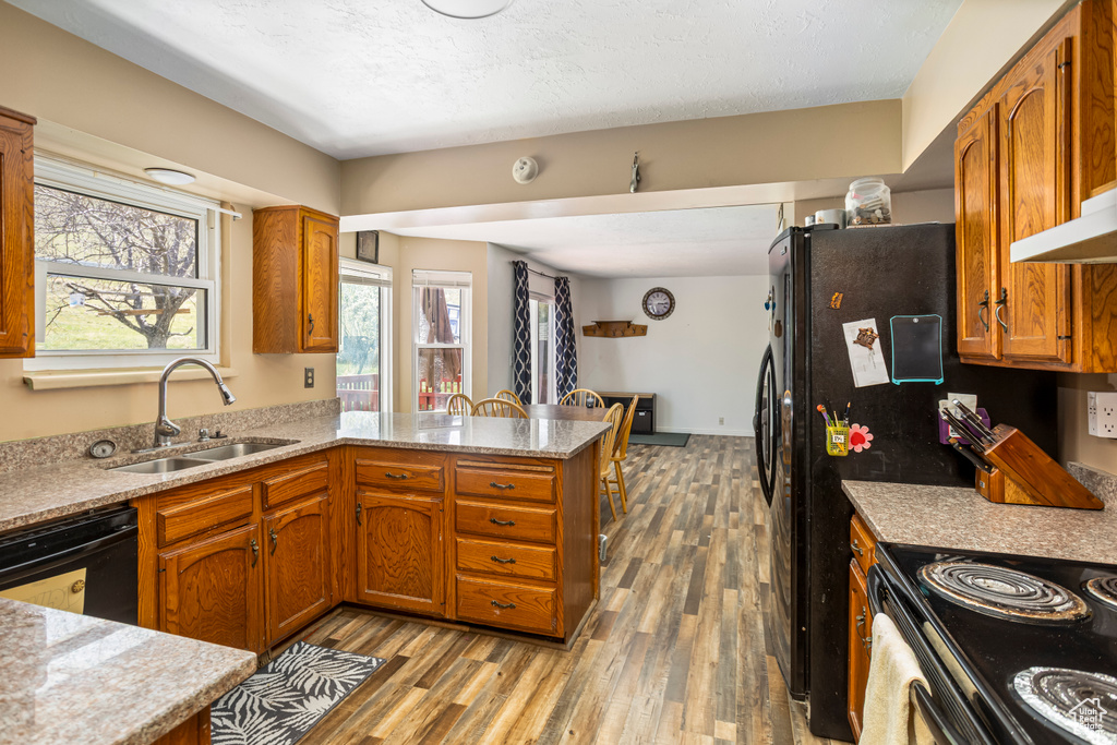 Kitchen with brown cabinets, a sink, light wood-type flooring, a peninsula, and dishwasher