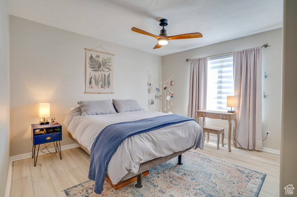 Bedroom featuring light wood-style flooring, a textured ceiling, baseboards, and ceiling fan