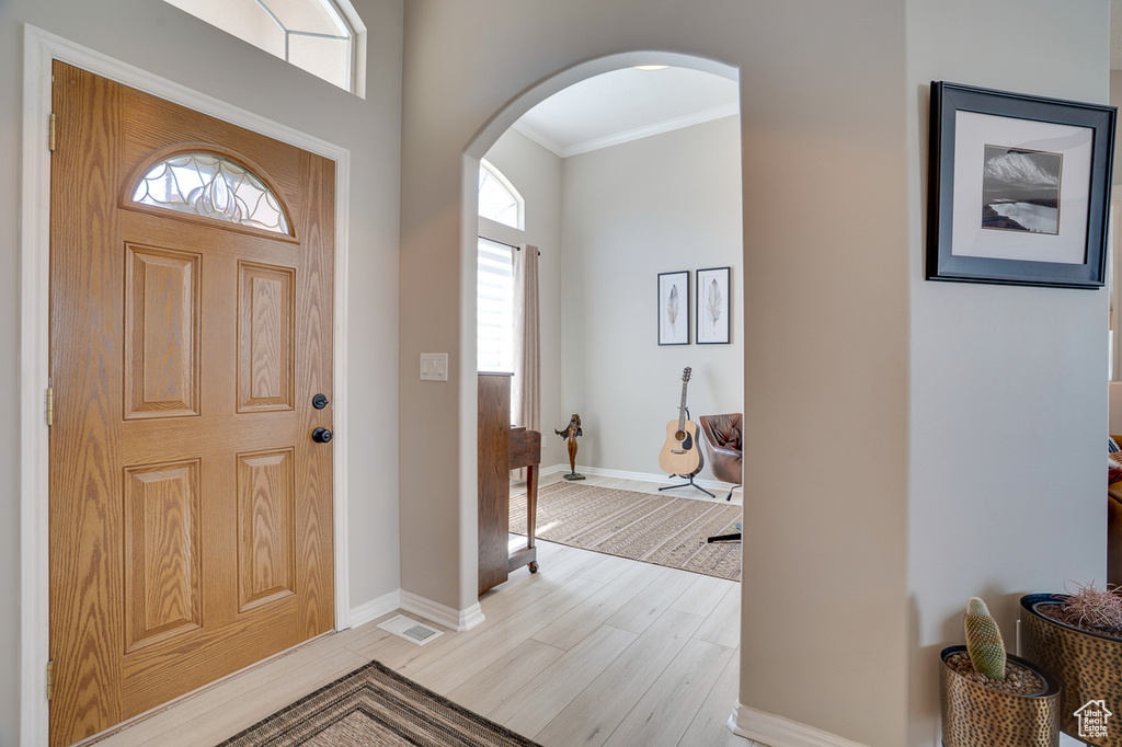 Entryway with arched walkways, crown molding, light wood-type flooring, and baseboards