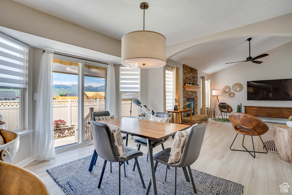 Dining room featuring light wood-type flooring, a stone fireplace, a ceiling fan, arched walkways, and lofted ceiling