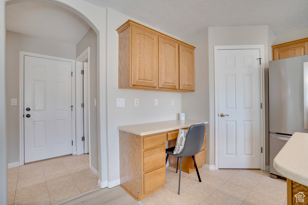 Office space featuring built in desk, light tile patterned floors, arched walkways, and baseboards