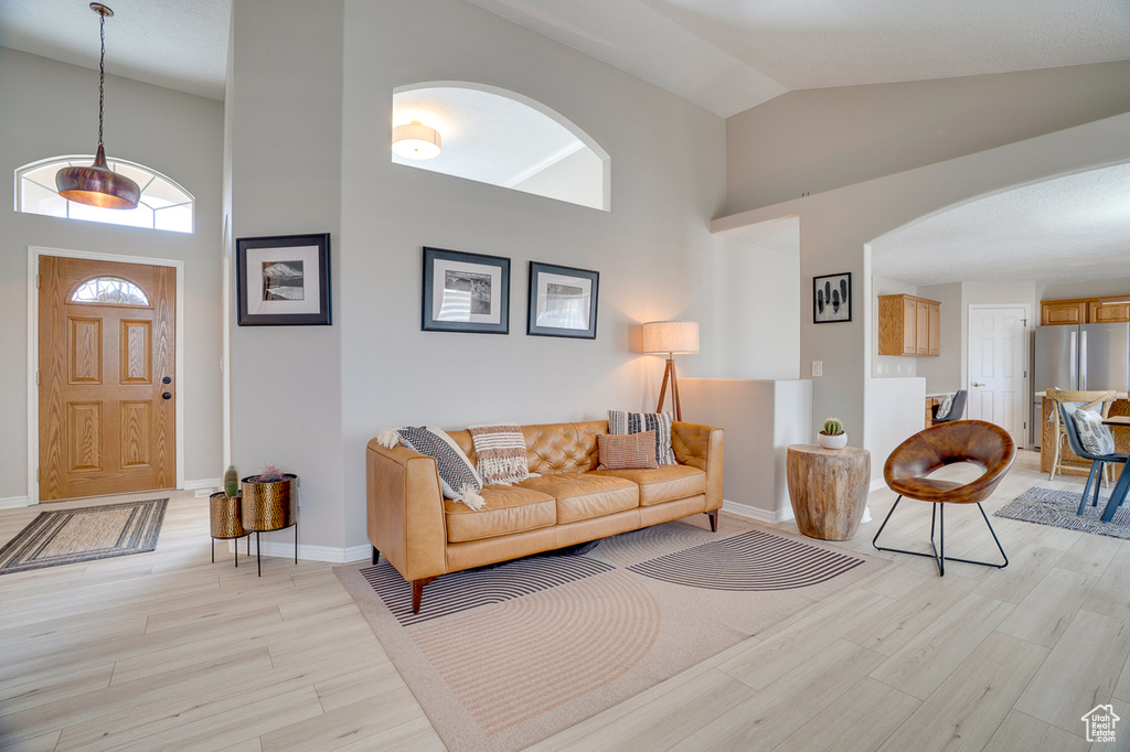 Living room with arched walkways, high vaulted ceiling, light wood-style floors, and baseboards