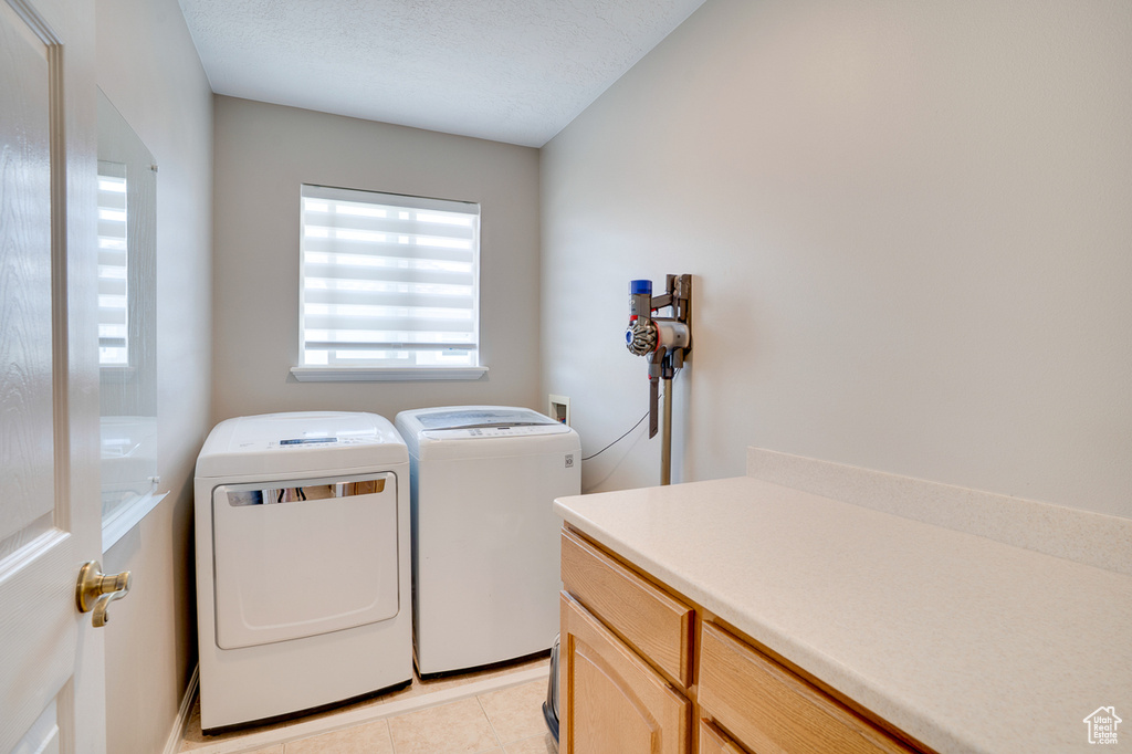 Laundry area with separate washer and dryer, cabinet space, and light tile patterned floors