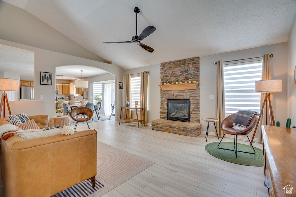 Living area featuring ceiling fan, arched walkways, light wood finished floors, vaulted ceiling, and a fireplace