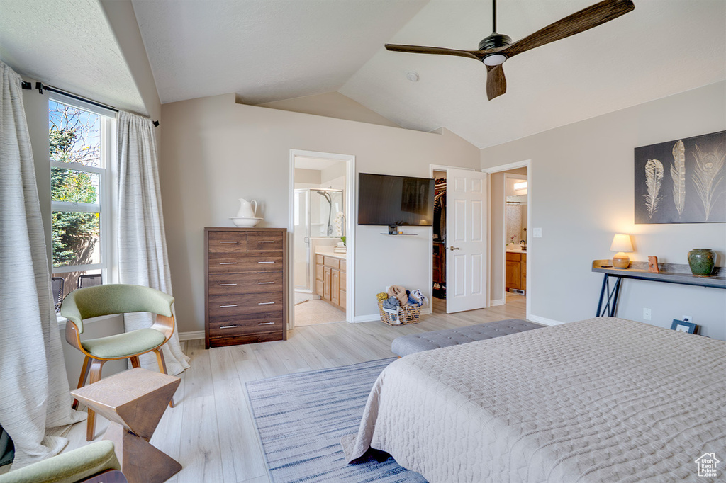 Bedroom featuring lofted ceiling, light wood-style floors, a walk in closet, ensuite bathroom, and baseboards