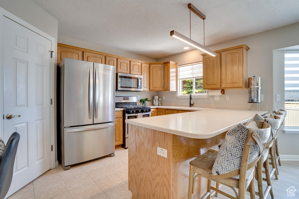 Kitchen with stainless steel appliances, a peninsula, a kitchen bar, light countertops, and a textured ceiling