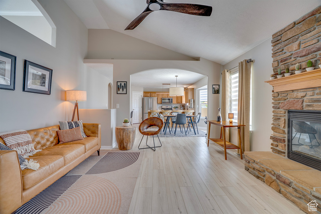 Living area with arched walkways, a ceiling fan, light wood-style flooring, vaulted ceiling, and a fireplace