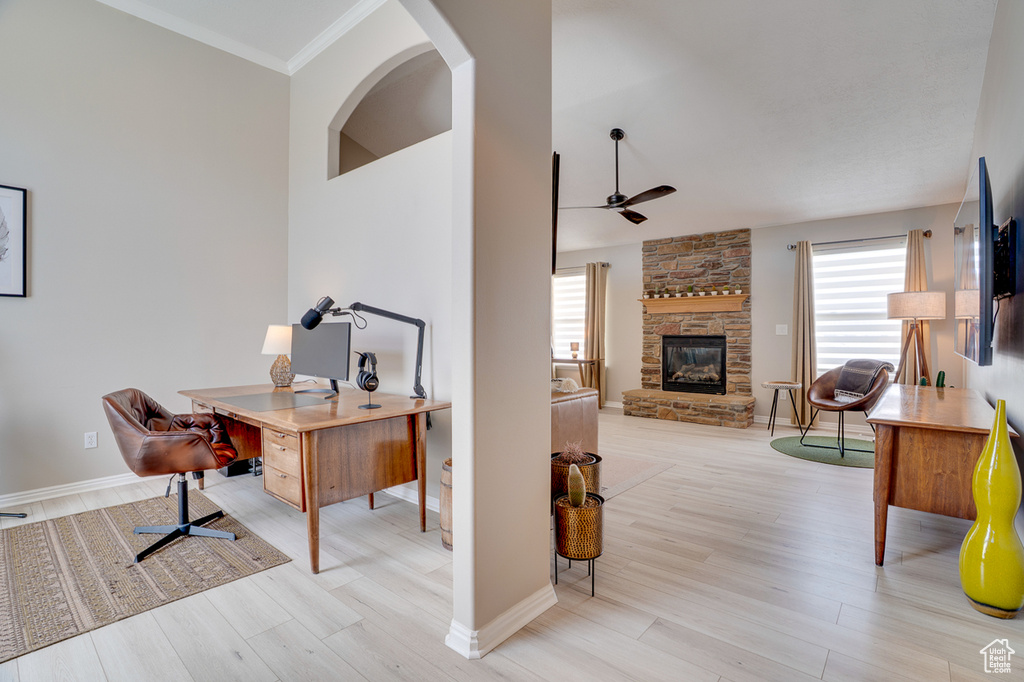 Office featuring a ceiling fan, healthy amount of natural light, wood finished floors, a stone fireplace, and ornamental molding