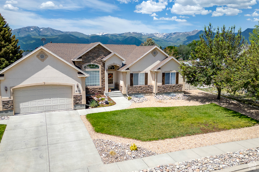View of front of house with stone siding, a mountain view, stucco siding, driveway, and an attached garage