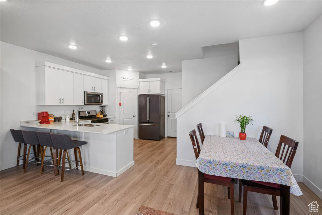 Kitchen featuring stainless steel appliances, a kitchen bar, light wood-style flooring, a peninsula, and baseboards