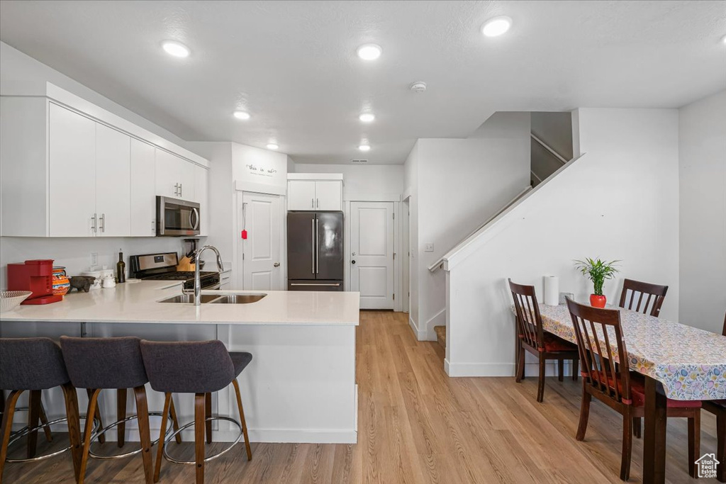 Kitchen featuring a breakfast bar, stainless steel appliances, light wood finished floors, a sink, and a peninsula